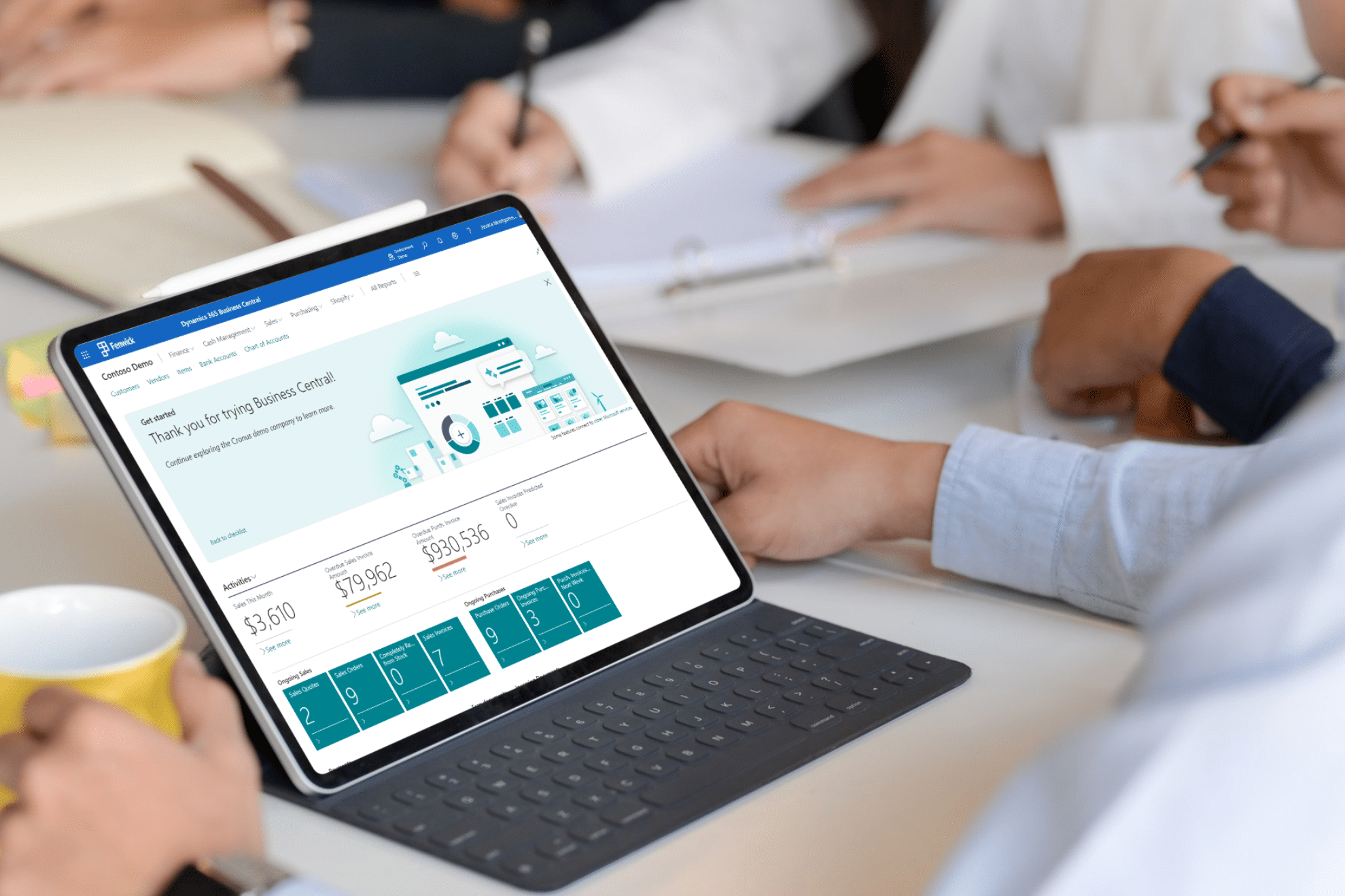 A person sits in a meeting with a laptop displaying the Microsoft Dynamics 365 Business Central interface on the screen