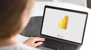 This is an image of the Microsoft Power BI loading screen on a laptop with a person working behind it.